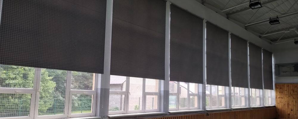 kilka rolet materiałowych na szkolnej sali gimnastycznej