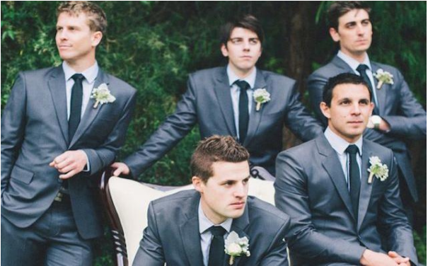 five men in dark blue-grey suits with white flowers on lapels