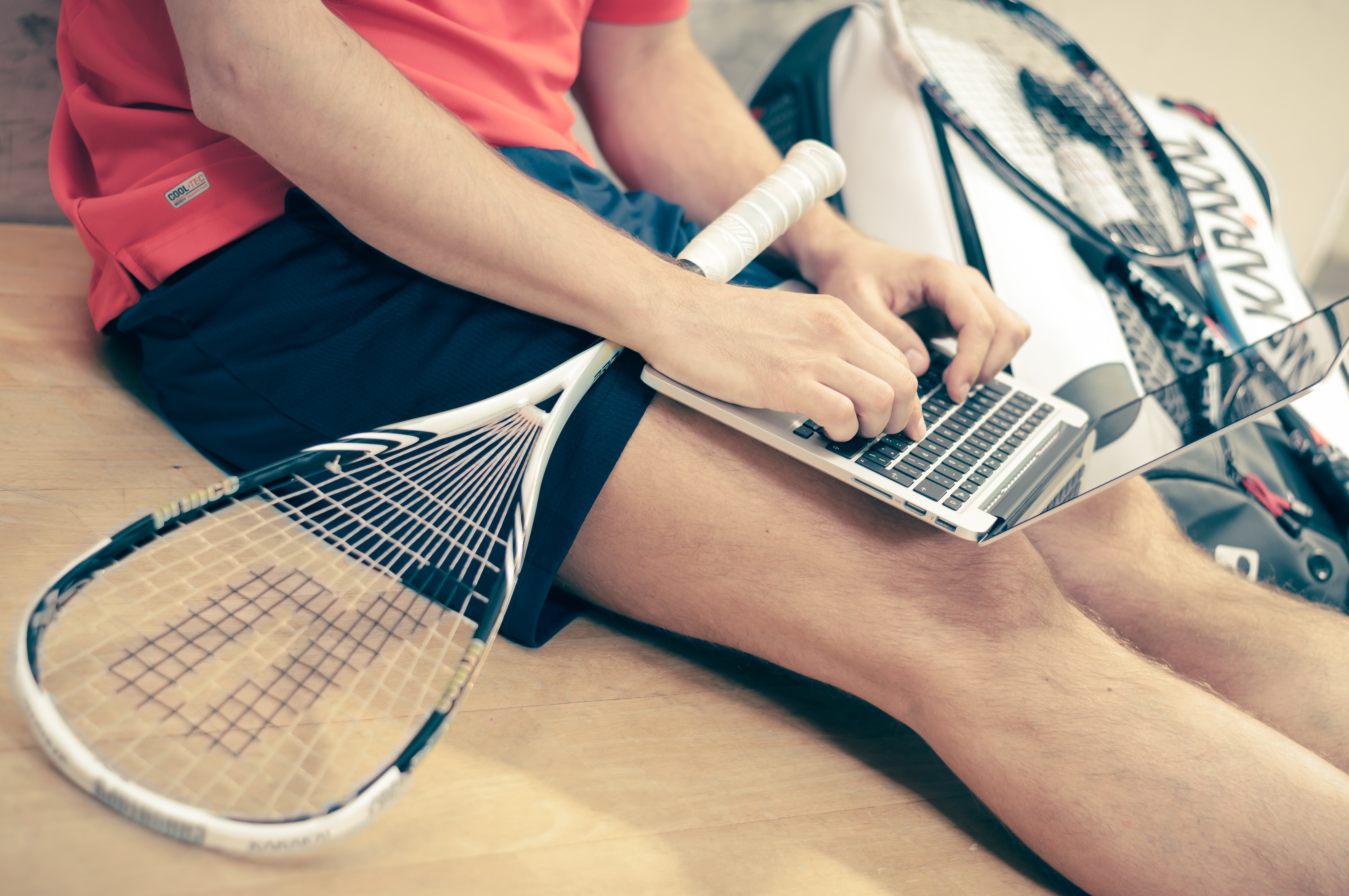 photograph picture of man with tennis racket typing into his laptop