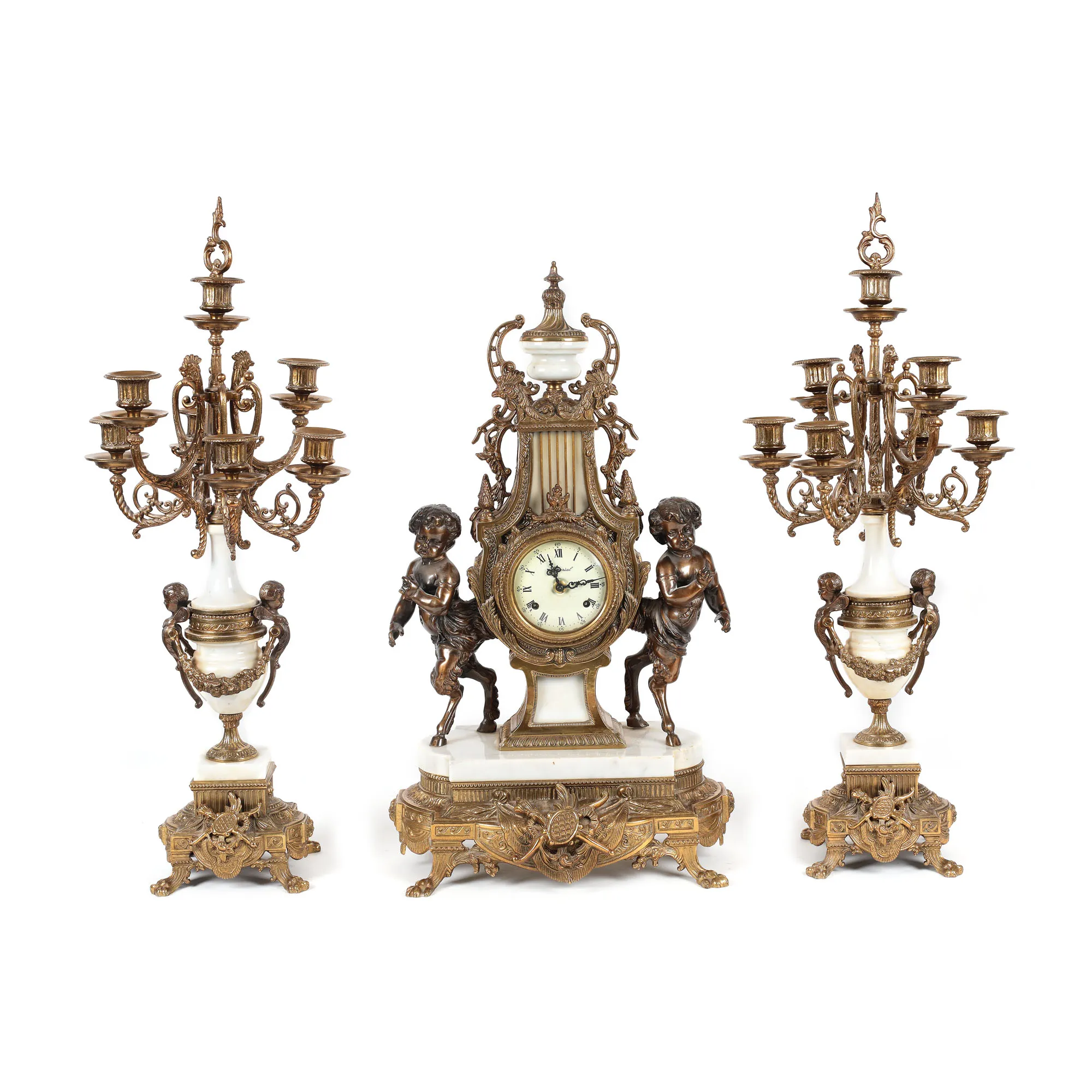 Garnitură Imperial Brevettato pentru șemineu, în manieră Louis XVI, formată din ceas Franz Hermle și două sfeșnice, din bronz și marmură, prima jumătate a sec. XX
