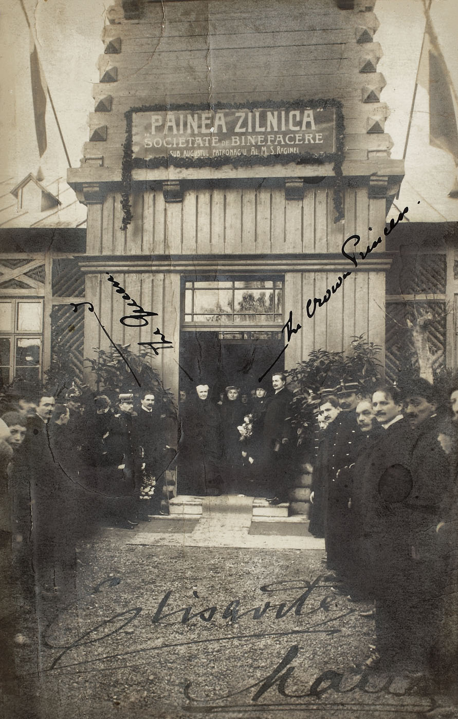 Carte poştală reprezentând-o pe Regina Elisabeta şi pe Principesa Maria a României în faţa Societăţii de Binefacere "Pâinea Zilnică", încadrată de o ramă de birou decorată cu Jubileul de 40 de ani al Regelui Carol I, 1908