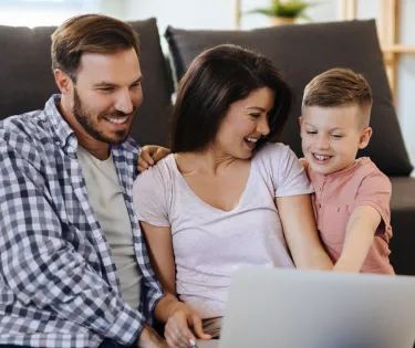 Immagine che raffigura un uomo, una donna e un bambino in soggiorno che guardano felici lo schermo di un computer