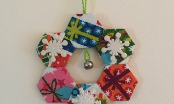 Six small hexagons are stuck together to create a snowflake shape. A small bell hangs in the centre of the shape. The shape is decorated with snowflakes