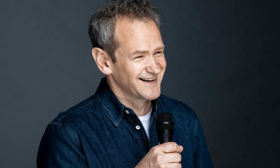 Alexander Armstrong smiling and holding a microphone. He looks beyond the camera.