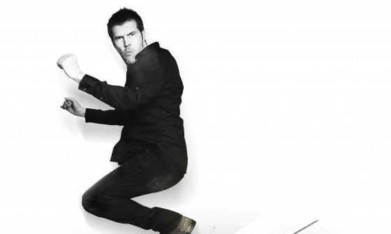 Rhod Gilbert is jumping over a large open book. The image is in black and white.