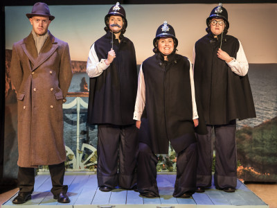 Four members of the Crimes-on-the-Coast cast wear costume aboard a deck. Three are dressed as policemen and one as a detective.