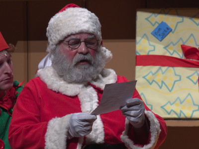 Santa reads a list as the elf reads over his shoulder