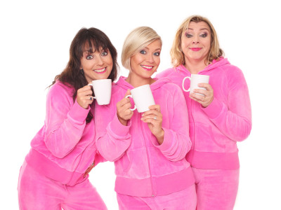 Three cast members stand in pink velour tracksuits with coffee mugs