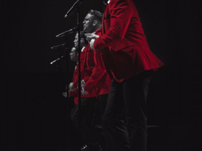 Bye Bye Baby perform on stage. The image is in black and white and their suit jacket is in red.