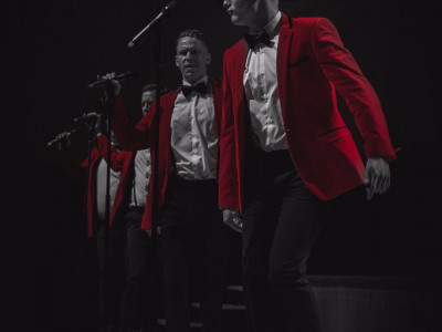 Bye Bye Baby perform on stage. The image is in black and white and just their suits are red.