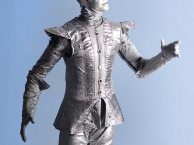 Tinman is standing up straight. He is turned to the side with his left arm raised
