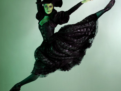 The Wicked Witch is leaping into the air. Her skin is coloured green and her dress is long and black