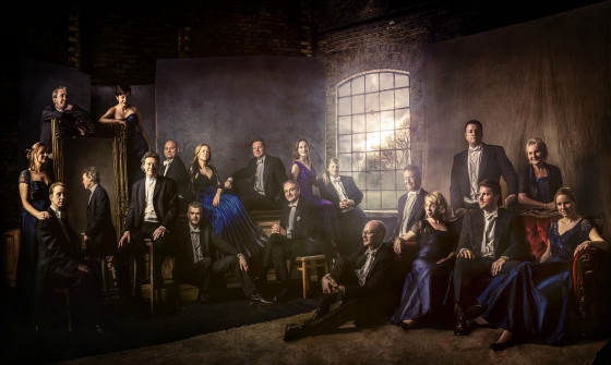 The Sixteen are sat in front of a window. The image is dark
