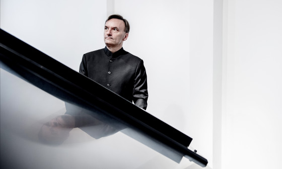 Stephen Hough is standing behind a piano looking up towards the ceiling