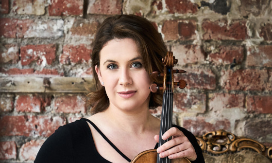 Chloë Hanslip is sat on a chair holding a violin on her lap.
