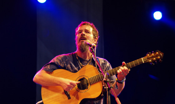 Keith James plays on stage at Glastonbury, holding a guitar and looking out beyond the camera.