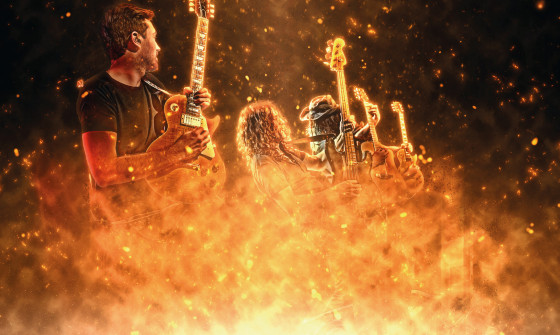 Guitarists stand behind a wall of flames. Ashes fly from the fire.
