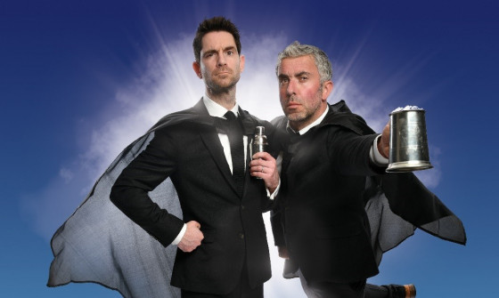 The two members of The Thinking Drinkers hold a tankard and a can, wearing suits and capes.