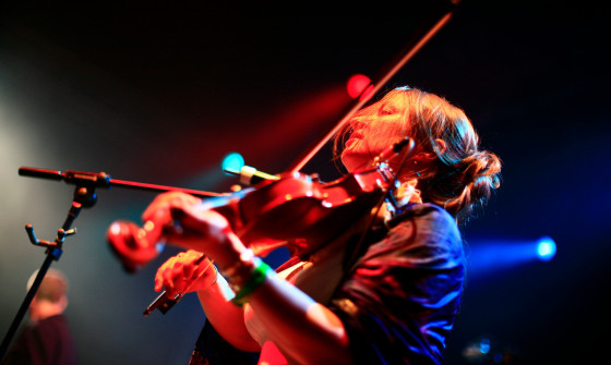 Eliza Carthy plays the violin on stage. She is under red lighting.