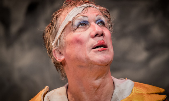 Peter Duncan looks up past the camera wearing blue eyeshadow and red lipstick.