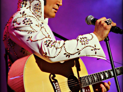 Ben Portsmouth performs on stage holding a guitar and a microphone