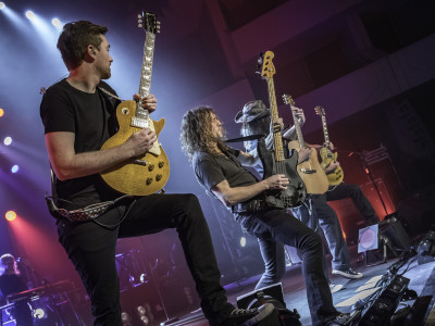 Four guitarists stand at the edge of the stage and play to the audience