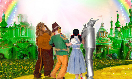 The Lion, the Scarecrow, Dorothy and the Tinman all stand on the yellow bring road facing a rainbow above the Emerald City.