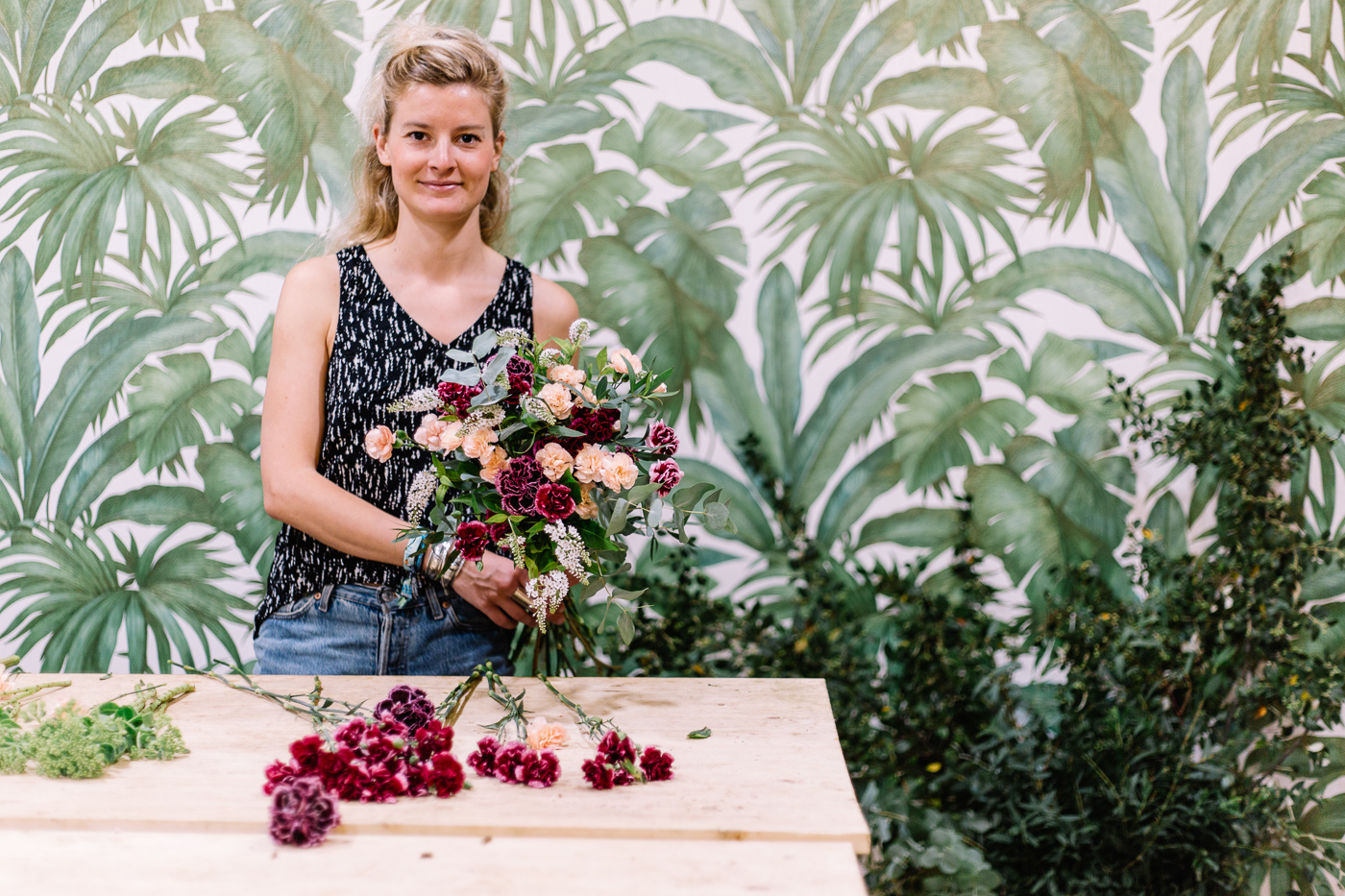 Emmanuelle Magnan de Pampa Paris présente un bouquet dans son atelier, devant un papier peint à feuilles vertes