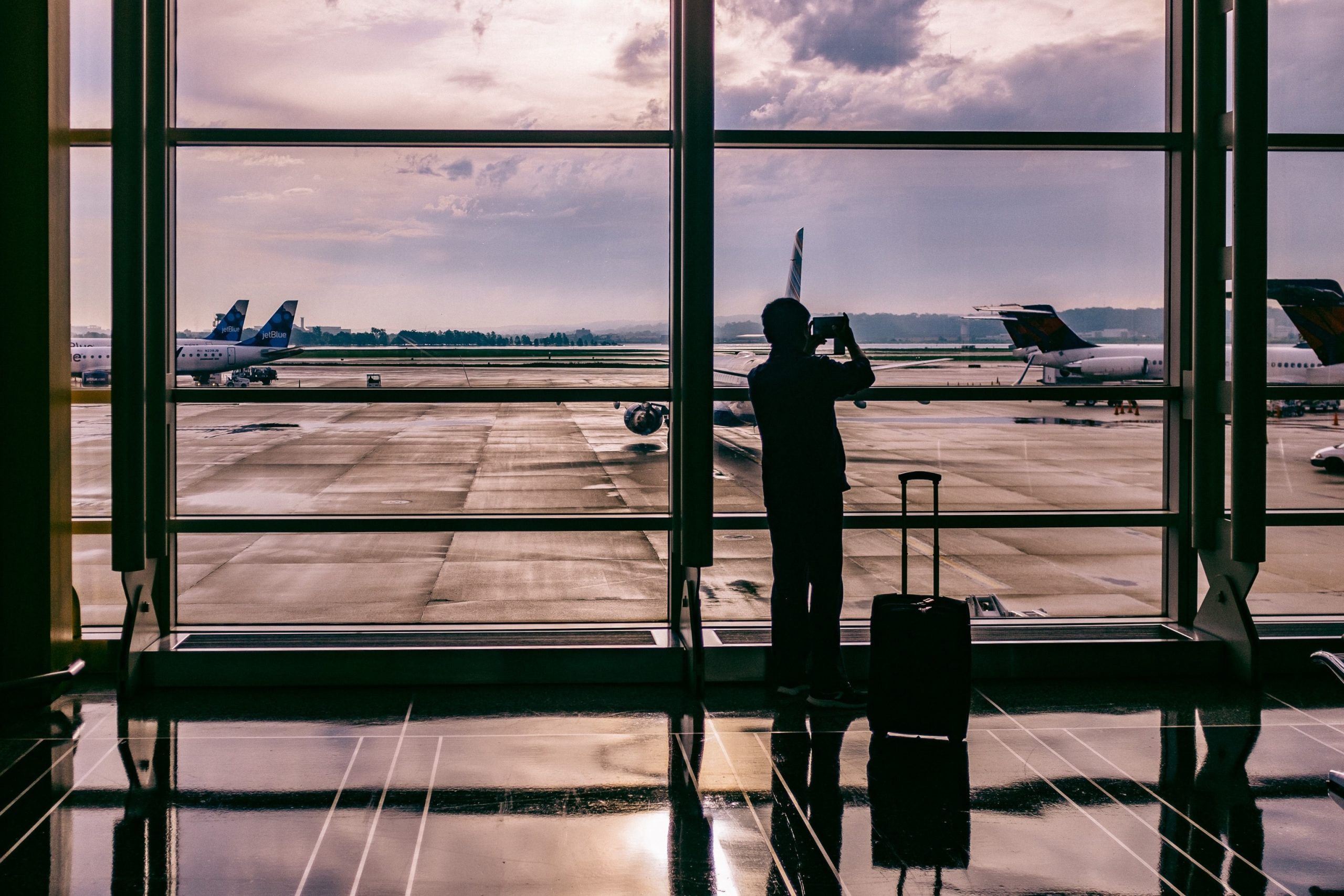 Photo of a traveller looking out of an airport window onto the planes parked outside with the sun low in the sky