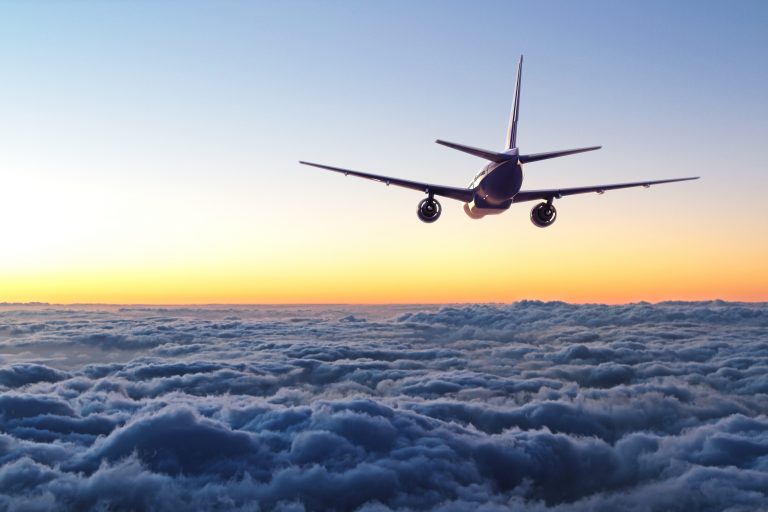 Plane flying above the clouds towards the sun which is low on the horizon line