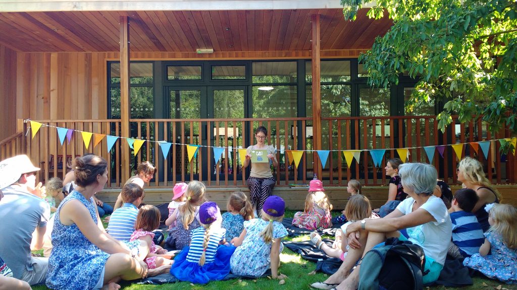 The Librarian reading to a large group of children and their guardians on the grass.