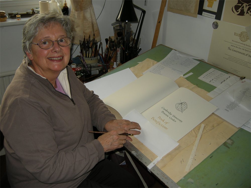 A calligrapher sitting at a desk, inscribing the Book of Benefactions.