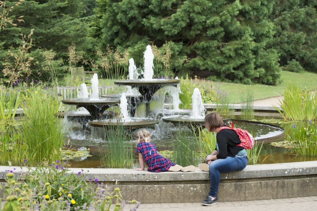 A woman and child sit on the edge of the fountain, looking in to the water.