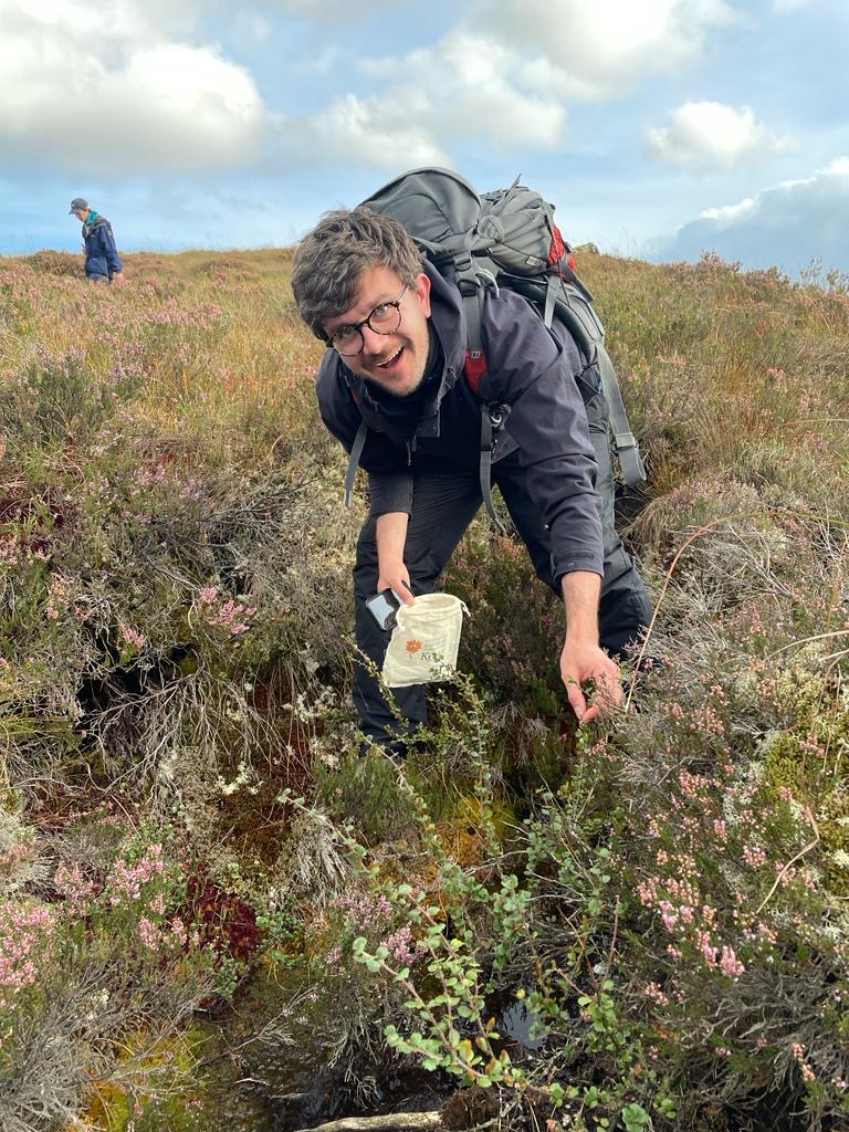A smiling man collects seed samples on a plant collecting expedition.