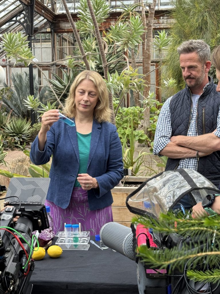 CUBG Director, Beverley Glover and BBC Gardeners' World Presenter, Nick Bailey in the CUBG Glasshouse Range looking at a test tube of blue liquid while being filmed