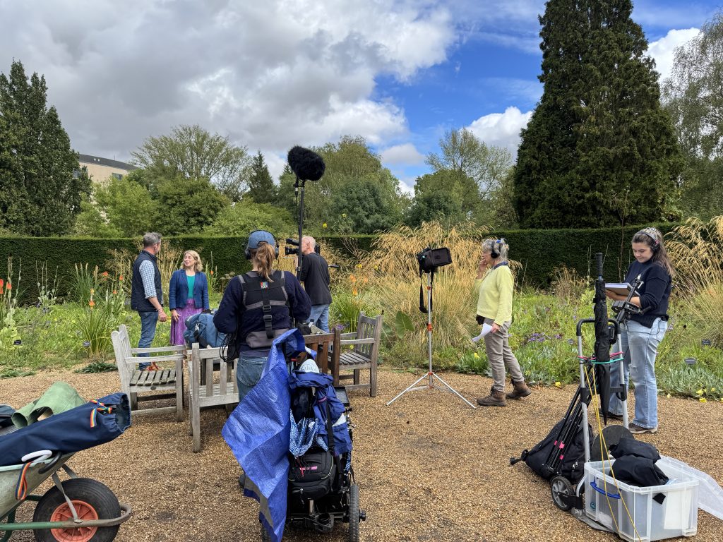 A film crew surround BBC Gardeners' World presenter Nick Bailey and Beverley Glover by the CUBG Dry Meadow