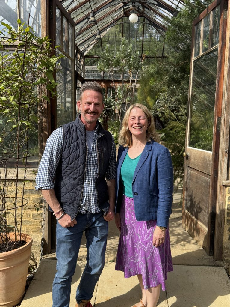 Gardeners' World presenter, Nick Bailey, and CUBG Director, Beverley Glover, standing together smiling outside the CUBG Glasshouse Range