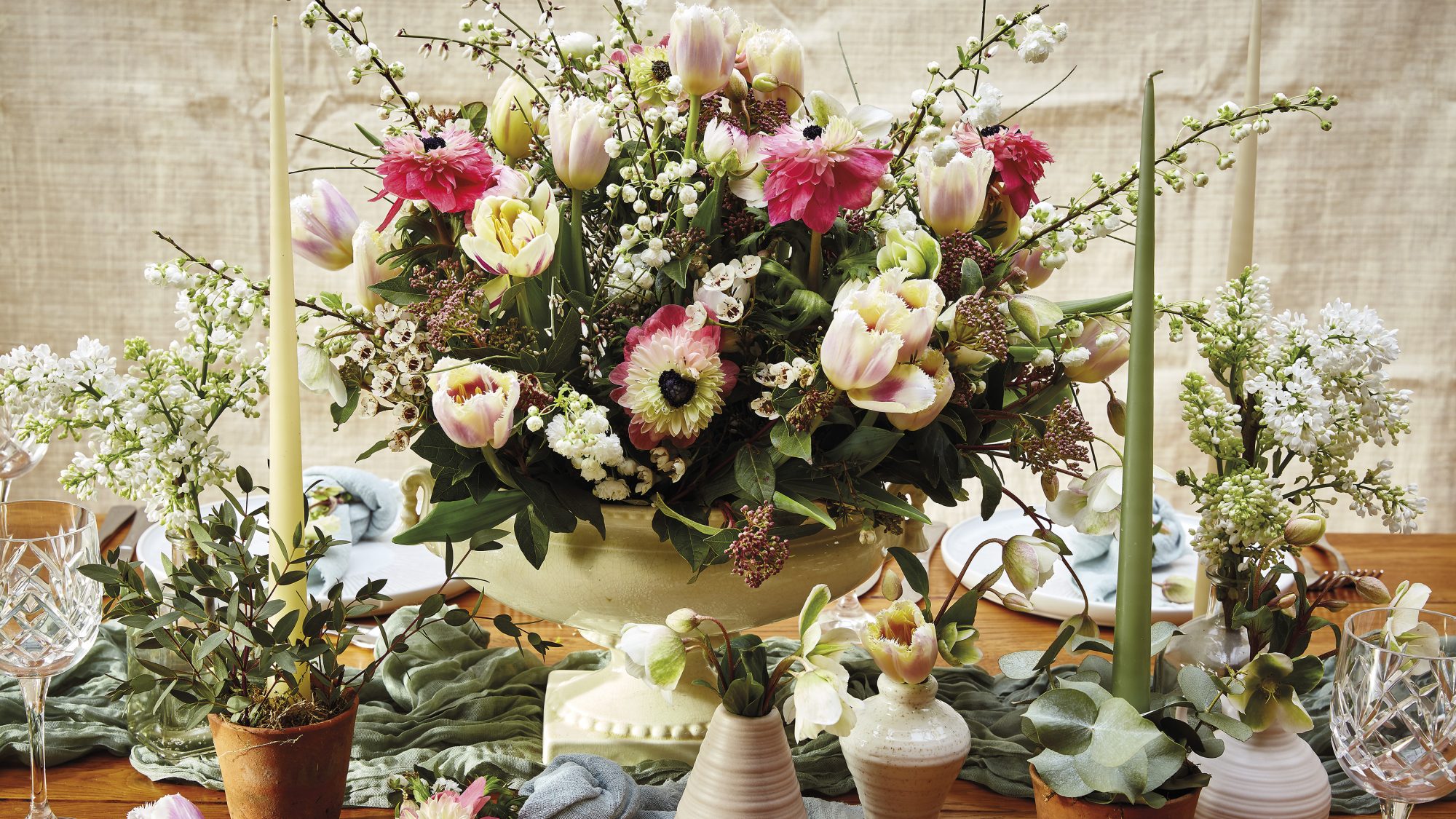 An centrepiece arrangement of pink and cream anemones on a table surrounded by candles and plates 