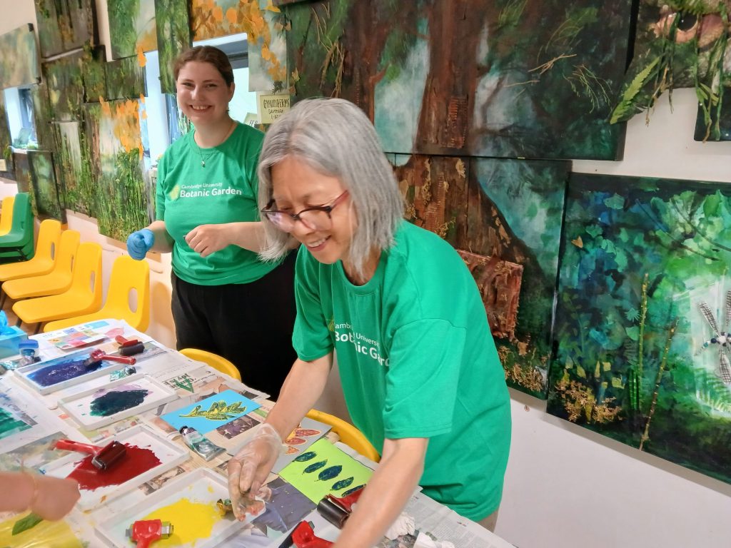 Two women smile as they prepare paints and painting materials in a classroom.
