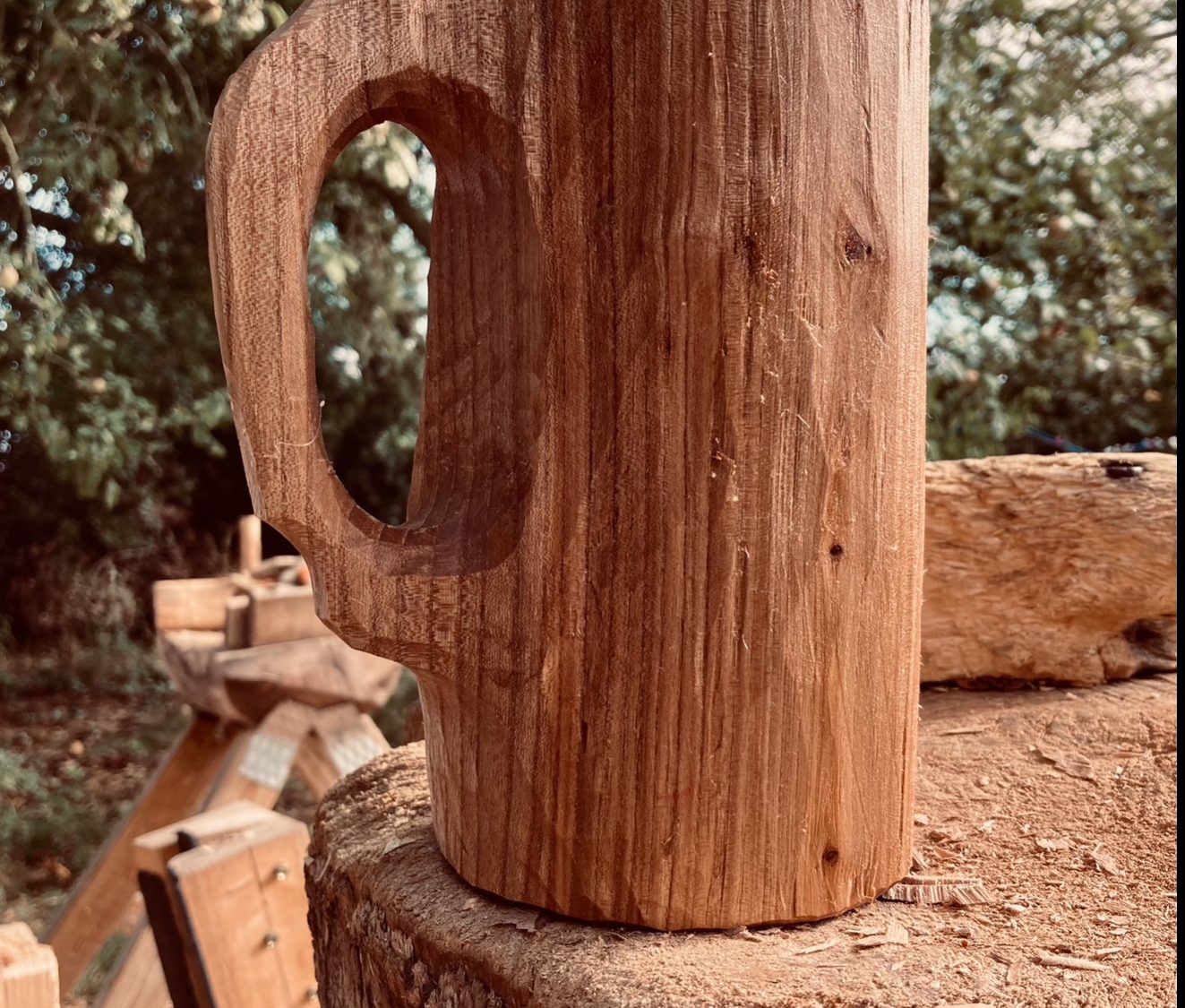 A tall, hand carved wooden drinking vessel with handle