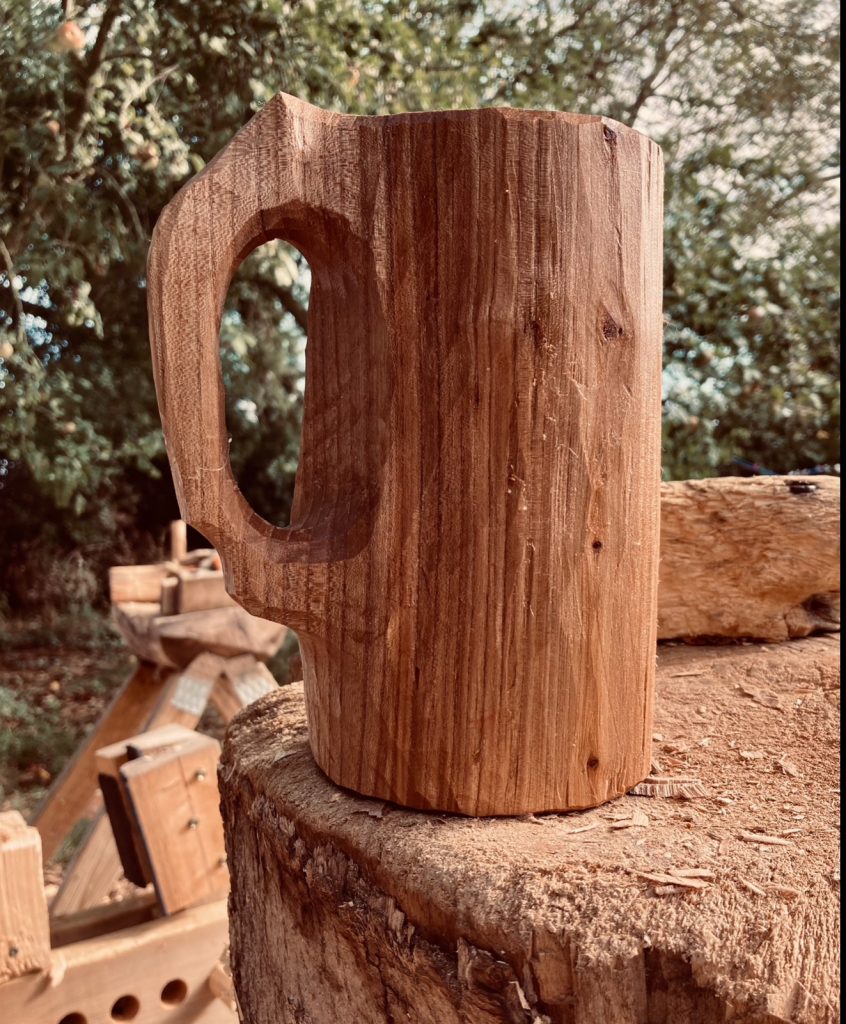 A tall, hand carved wooden drinking vessel with handle