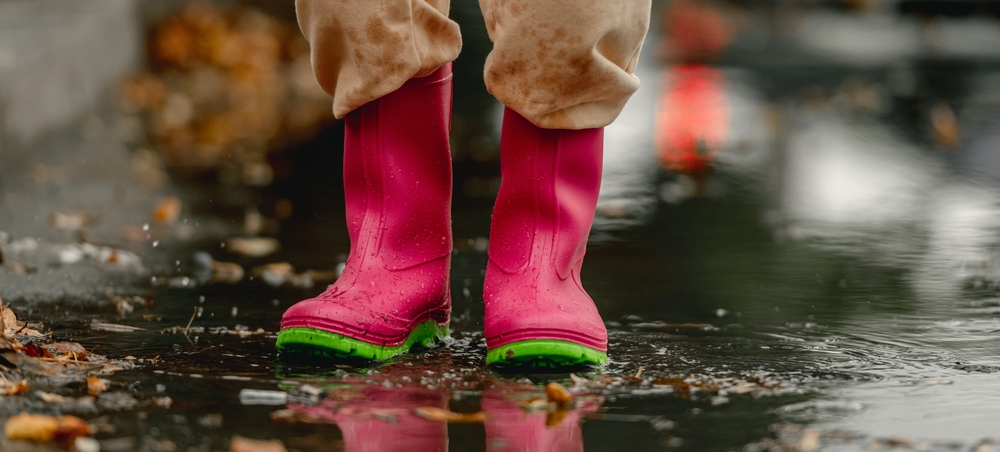 Child wearing pink welly boots splashing in a puddle.