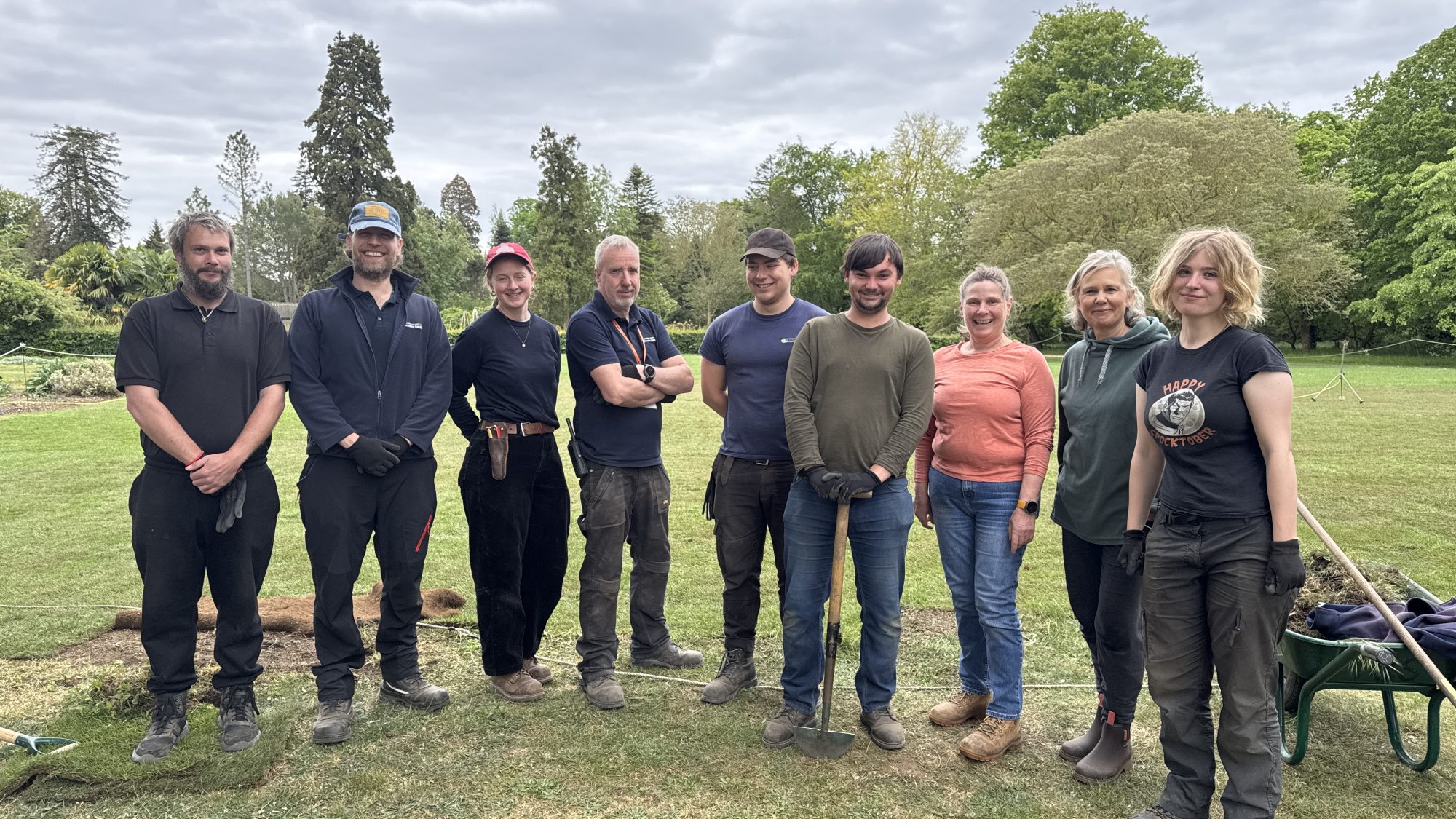 A group of people stands in a field, holding various tools, engaged in an outdoor activity or project.