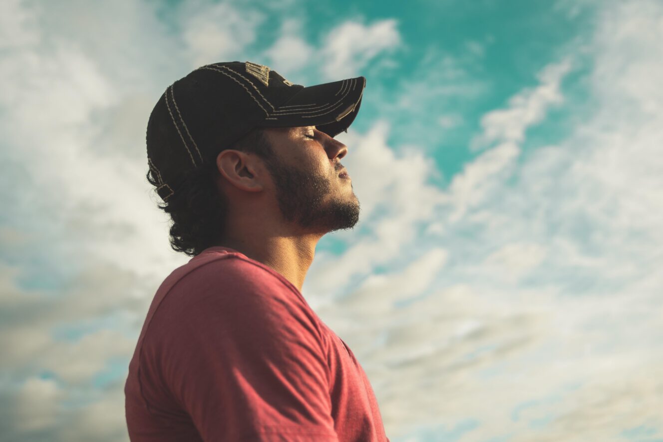 Man wearing black cap with eyes closed under cloudy sky 810775