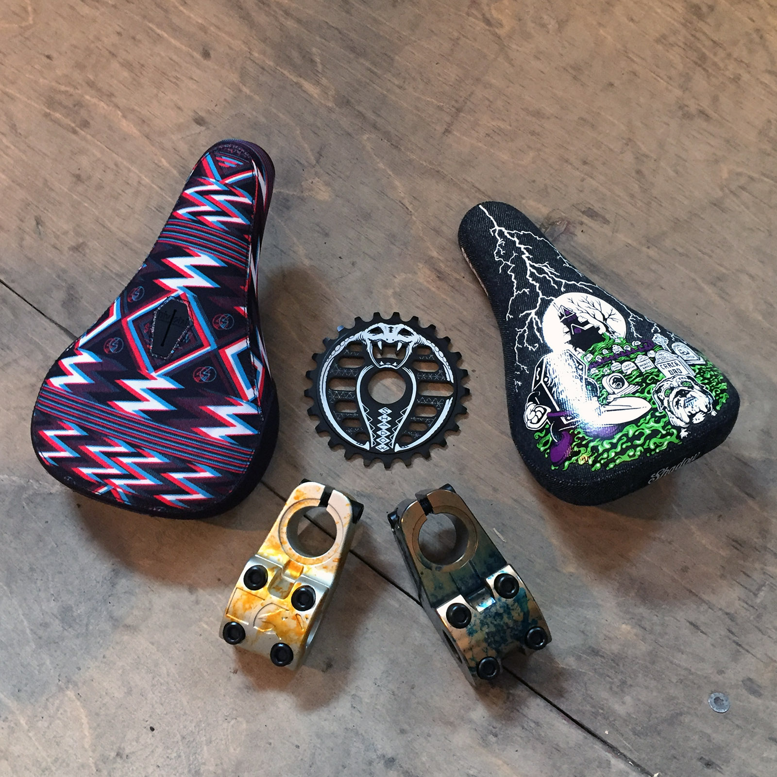 Dürfen wir vorstellen: Mark Burnetts (links), und Trey Jones Sognaturesättel (rechts) von The Shadow Conspiracy. Dazwischen haben wir das Kobra Sprocket und gleich darunter den Odin-Vorbau im Agent-Orange-Colorway sowie den Ravager-Toploader im Oil-Spill-Colorway