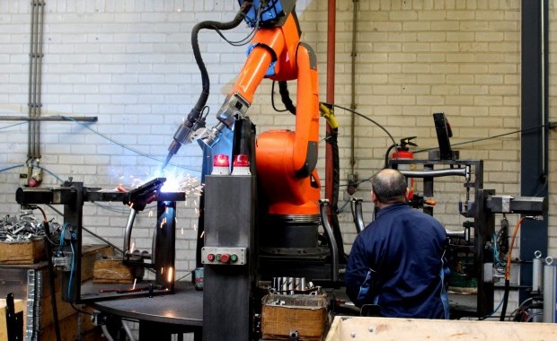 Ein Tacx-Mitarbeiter und der abgebildete Roboter arbeiten zusammen, um den Rahmen eines Heimtrainers zu verschweißen.