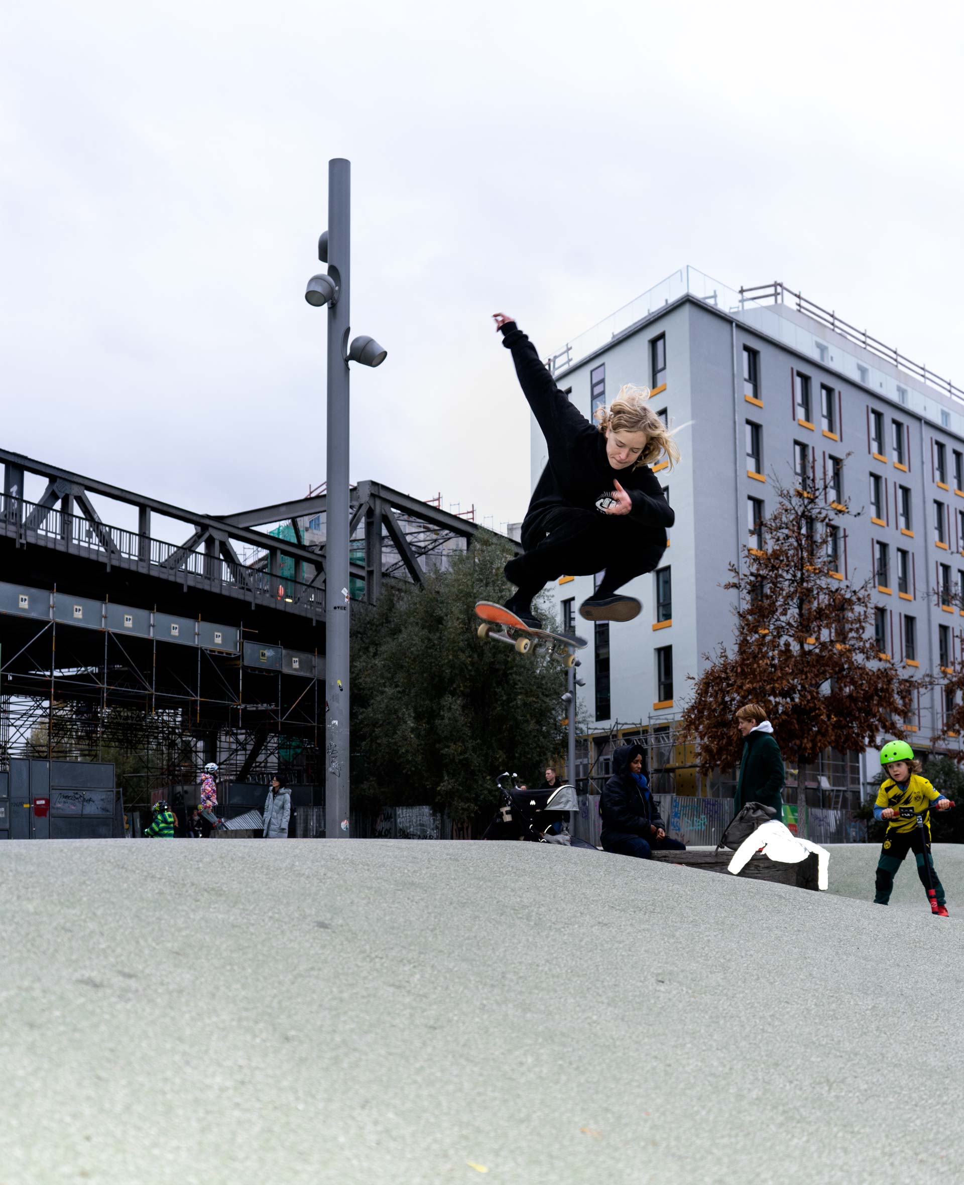 Julia mit einem Hardflip am Gleisdreieck, im Hintergrund spielen Kinder 