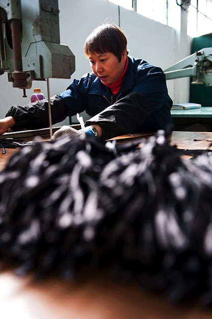 Mein Blick schweift von den bestickten Handschuhteilen quer durch die Halle. Das Geräusch einer kreischenden Säge hat meine Aufmerksamkeit erweckt. An einer Stichsäge sitzend sehe ich eine andere Chinesin, die unablässig Handschuhbändel auf die richtige Länge zuschneidet; vor ihr liegend türmt sich ein Haufen bereits zugeschnittener Bändel auf. Ich bin beeindruckt: wirklich jedes Detail am späteren Handschuh scheint von Hand zugeschnitten und bearbeitet. Vollautomatische Maschinen in der Fabrik gibt es nicht. 