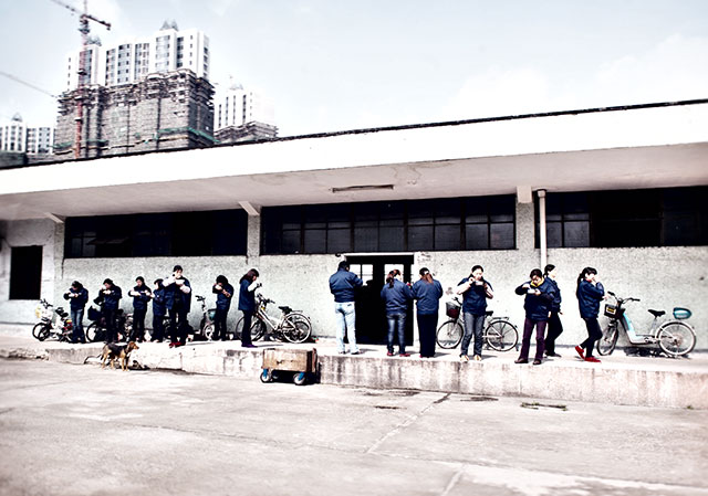 Ausgelassen miteinander tratschend laufen die Näherinnen an mir vorbei zur firmeneigenen Essensausgabe vor der Fabrik. „Das wäre vor 30 Jahren noch nicht denkbar gewesen“, fügt Shin zufrieden über die enorm verbesserten Arbeitsbedingungen an. Vor der Fabrik stehend schlürfen die chinesischen Arbeiterinnen ihre wohlverdiente Nudelsuppe. Im Hintergrund sieht man Kräne, welche einen mit Baugerüsten umhüllten Wolkenkratzer aus dem Boden stampfen. Sinnbild für ein Land im Aufbruch.