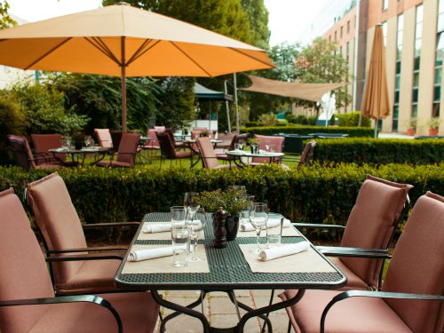 Vier Stühle rund um einen gedeckten Tisch im Garten des Imperial Riding School Vienna Hotel